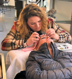 Gaia Salon in Manhattan, KS - In a serene salon, a woman expertly applies lash extensions to another, enhancing her natural beauty while she lies back and enjoys the luxurious treatment.